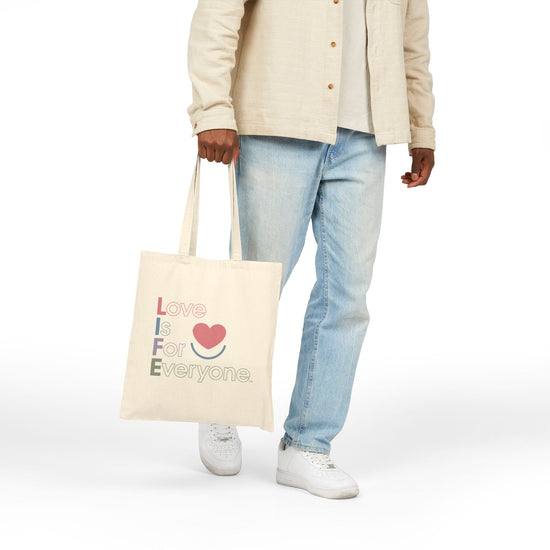 Hand holding natural Color Pop canvas tote by the handles, heart print message.