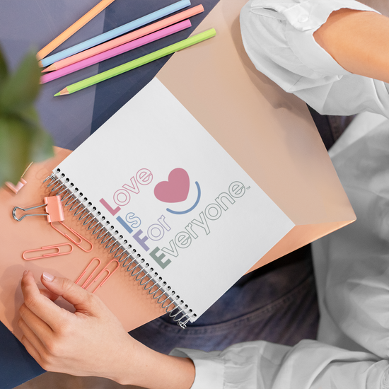Notebook with Color Pop "Love is for Everyone" cover on desk with model.