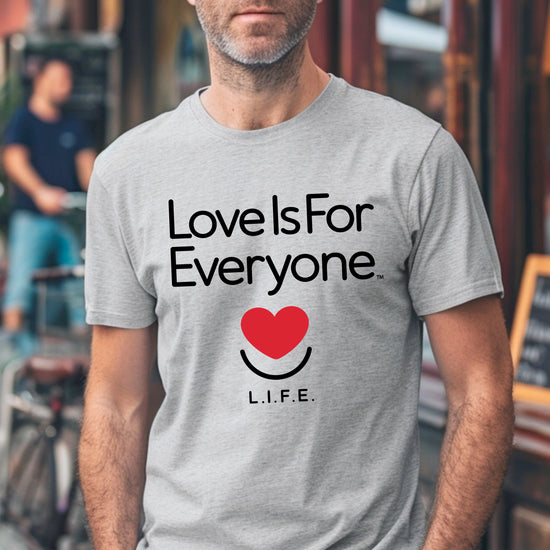 Man wearing men's grey Classic Tee, front view of "Love is for Everyone" message and smiling heart logo.