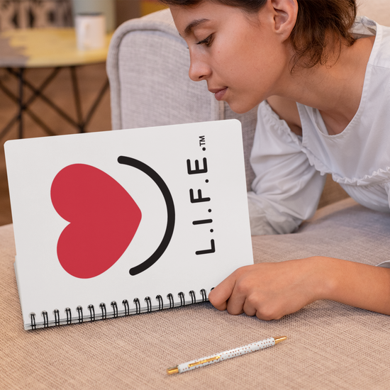 Woman holding a notebook open with L.I.F.E. heart smile logo on cover.