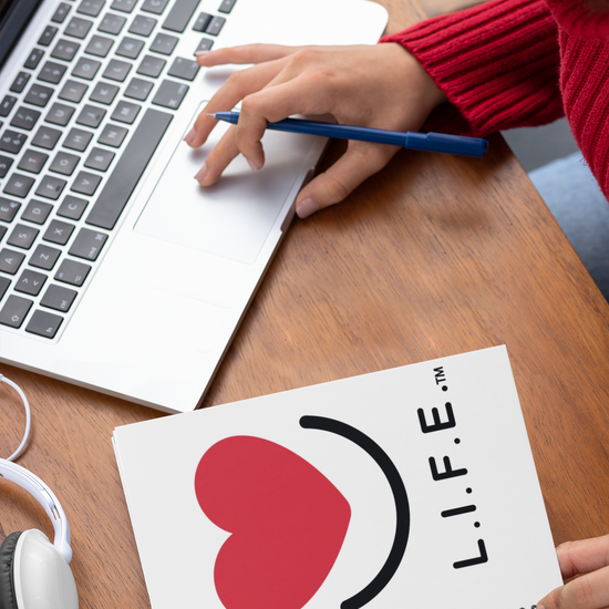 Person using a laptop with a L.I.F.E. "Love is for Everyone" spiral notebook with heart smile.