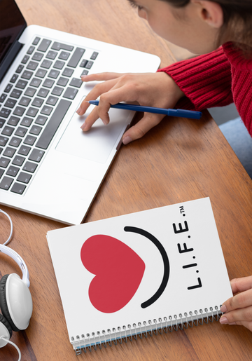 Person using a laptop with a L.I.F.E. "Love is for Everyone" spiral notebook with heart smile.