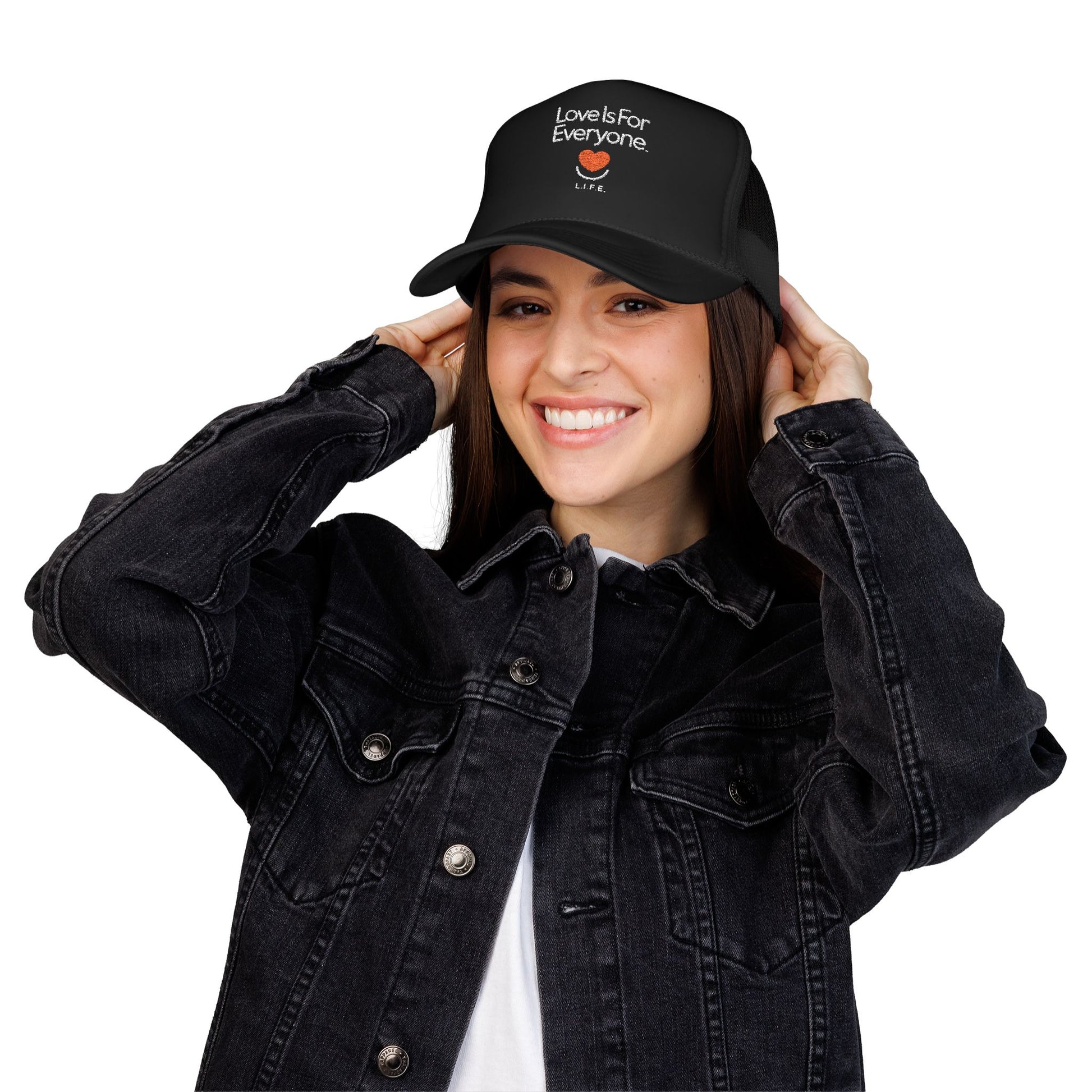 Woman wearing black L.I.F.E. embroidered "Love is for Everyone" trucker hat and smiling heart logo.