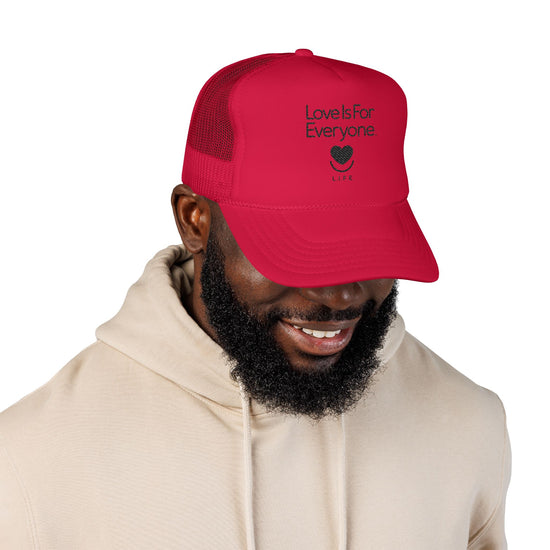 Man wearing red L.I.F.E. embroidered "Love is for Everyone" trucker hat with smiling heart logo.