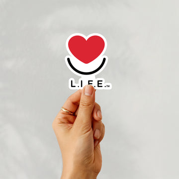 Hand holding L.I.F.E. "Stick with Love" 4x4 vinyl sticker with heart and smile logo.