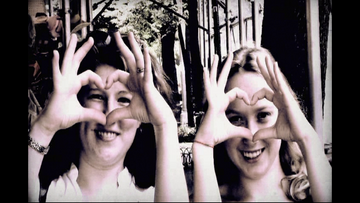 Two women making heart shapes with their hands outdoors.