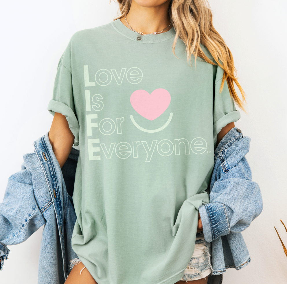 Woman wearing Bay pigment-dyed Comfort Colors ® tee with "Love is for Everyone" heart graphic.