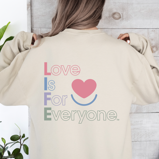 Woman wearing Color Pop back view showing vertical "Love is for Everyone" print on women's sand crewneck.
