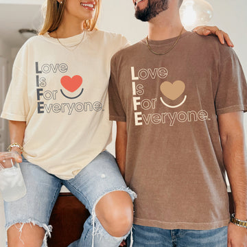 Couple wearing Colorful Expressions Tee in ivory and espresso, front view of vertical "Love is for Everyone" design in toned colors to coordinate with garment. 
