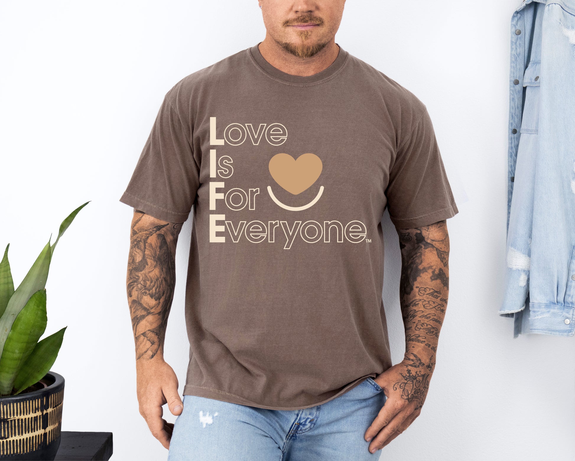 Man wearing a Comfort Colors espresso t-shirt with 'Love is for Everyone' text, standing against a white wall. 