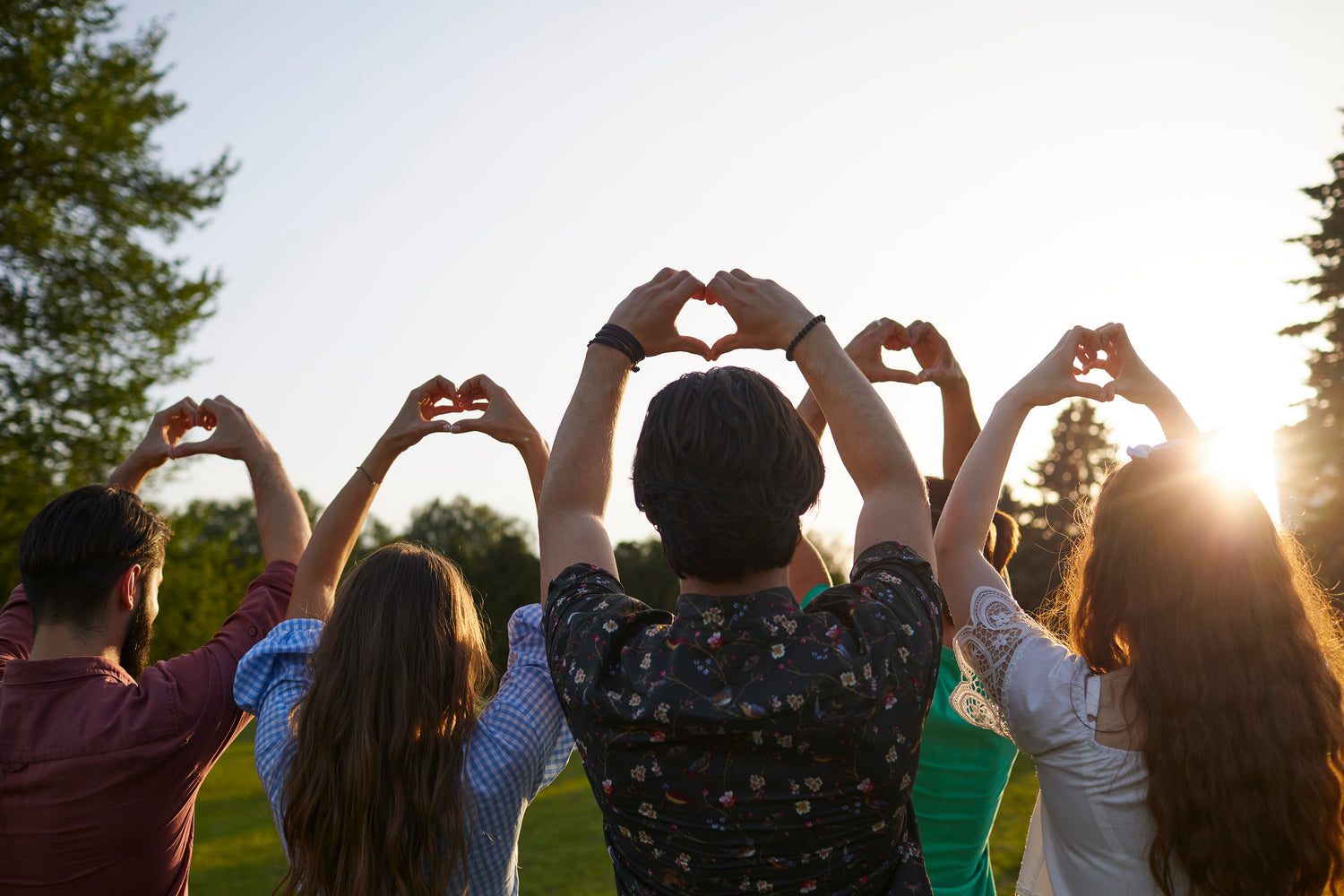 Group of people making heart shapes with their hands outdoors.
