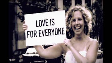 Woman holding a sign that reads 'Love is for Everyone' in an outdoor setting.