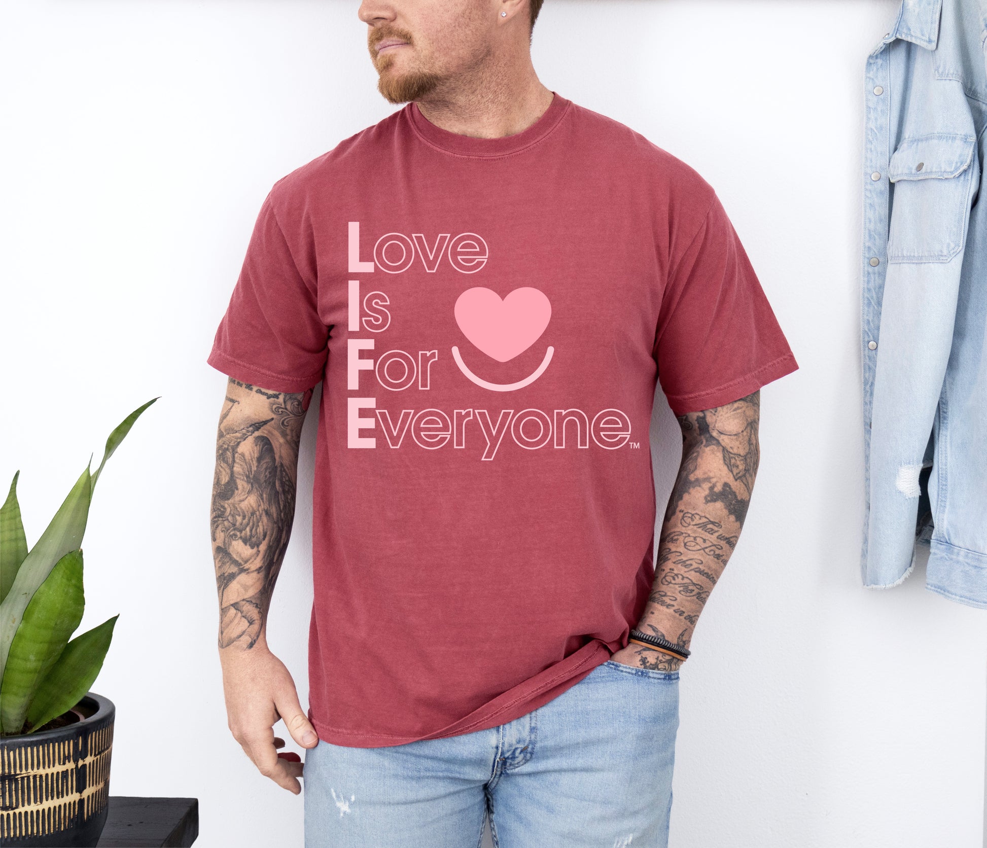 Man wearing Comfort Colors washed denim t-shirt with 'Love is for Everyone' text and heart symbol, standing against a white wall 