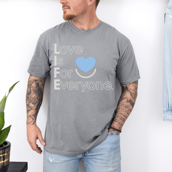Man wearing Comfort Colors gray t-shirt with 'Love is for Everyone' text and blue heart symbol.