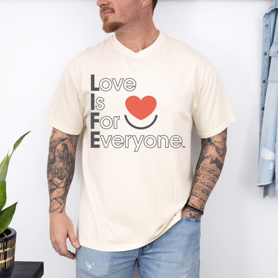 Man wearing men’s ivory Comfort Colors Tee with vertical muted Love is for Everyone message and heart smile logo. 