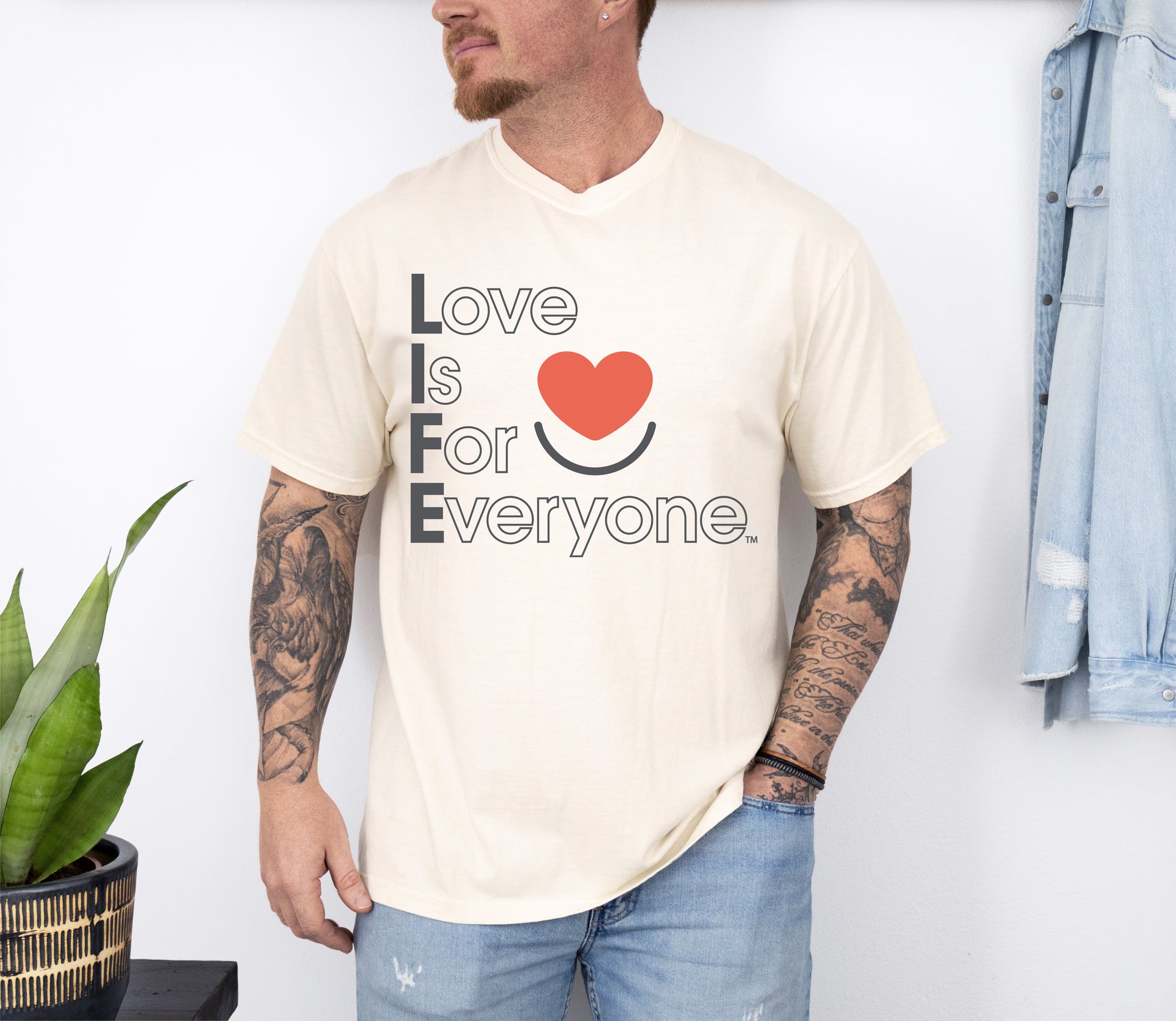 Man wearing men’s ivory Comfort Colors Tee with vertical muted Love is for Everyone message and heart smile logo. 