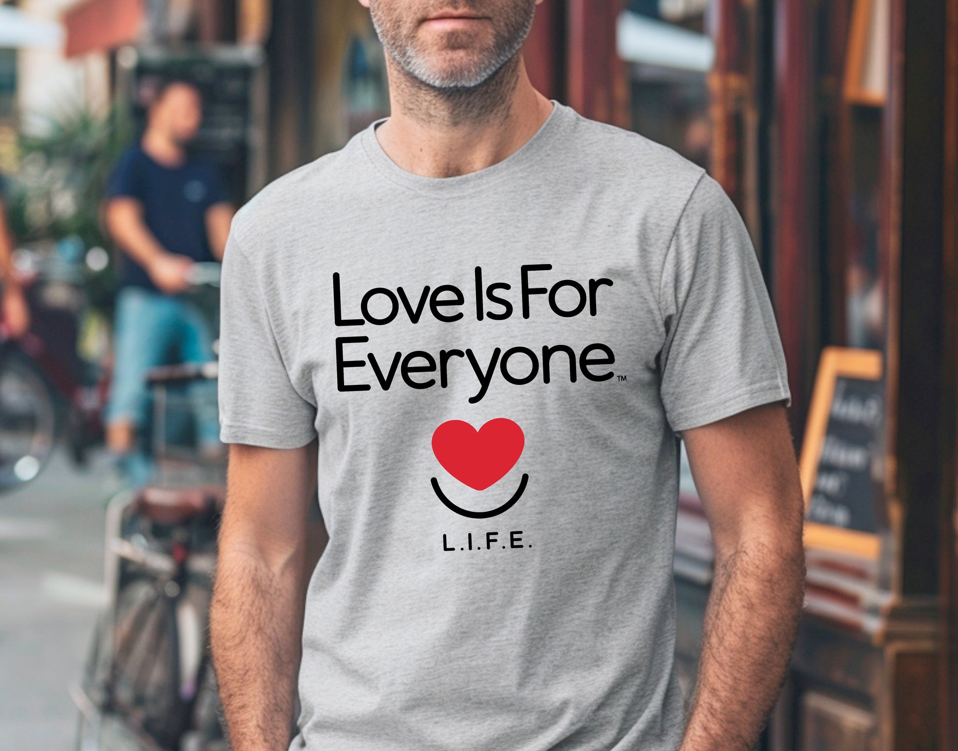 Man wearing men's grey Classic Tee, front view of "Love is for Everyone" message and smiling heart logo.