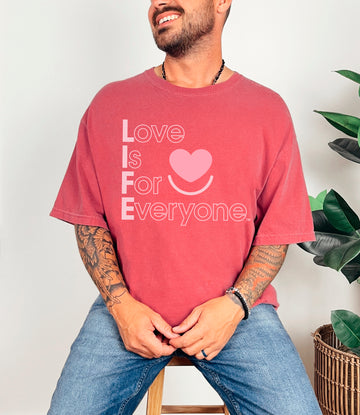 Men's/unisex Colorful Expressions Tee Crimson pigment-dyed, front view, vertical "Love is for Everyone" message in muted vintage look. 