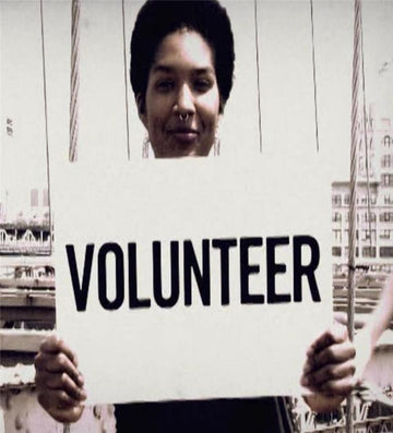 Woman holding a sign reading "Volunteer" in outdoor setting, 