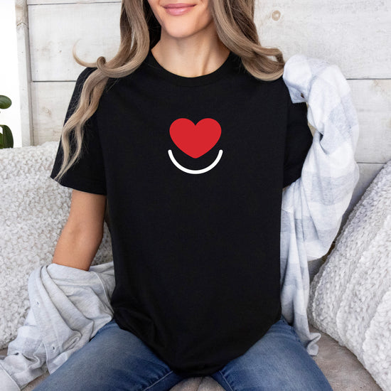 Woman in black L.I.F.E. Signature women's  graphic tee front with heart logo, seated casually. 