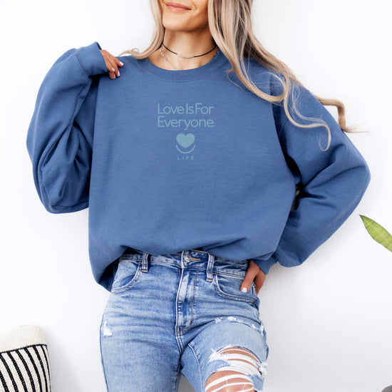 Woman wearing indigo blue L.I.F.E. Soft Spoken Tonal crewneck with subtle heart logo and "Love is for Everyone".