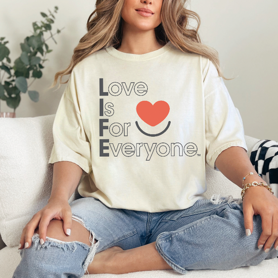 Woman wearing ivory Comfort Colors®  tshirt with red heart and muted vertical "Love is for Everyone" message. 
