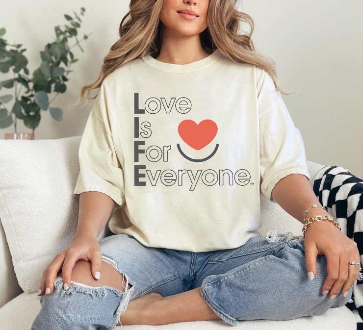 Woman wearing ivory Comfort Colors®  tshirt with red heart and muted vertical "Love is for Everyone" message. 