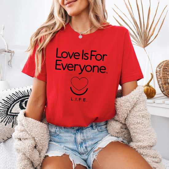 Woman wearing red L.I.F.E. "Love is for Everyone" classic women's T-shirt, relaxed pose. 