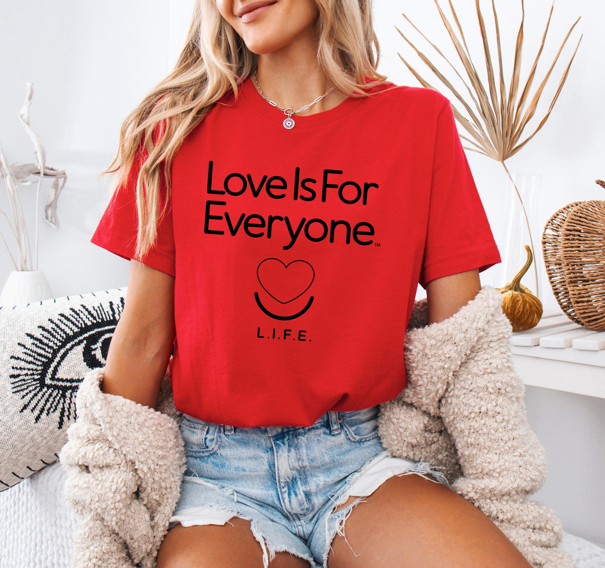 Woman wearing red L.I.F.E. "Love is for Everyone" classic women's T-shirt, relaxed pose. 