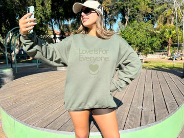 Woman wearing women's Soft Spoken Tonal Crewneck, front view of toned down classic "Love is for Everyone" message and heart smile design.