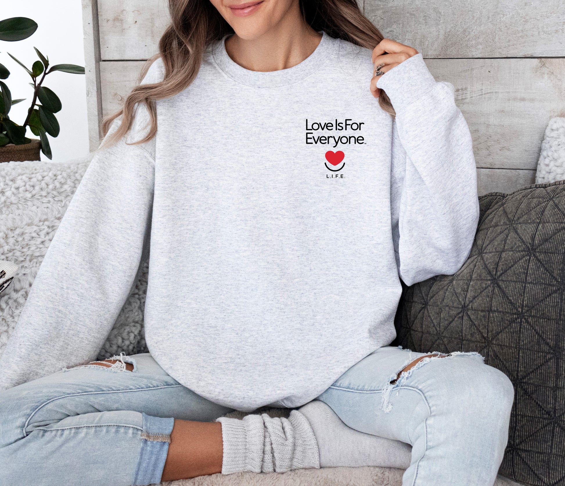 Woman wearing Subtly Stated crewneck ash with left chest logo “love is for everyone”. 