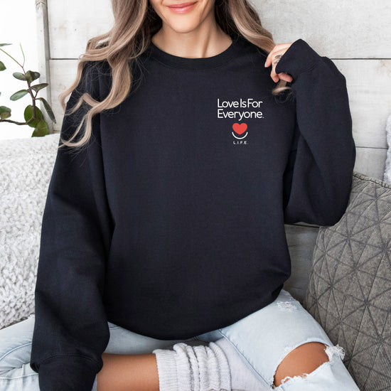 Woman wearing black L.I.F.E. Subtly Stated crewneck with small left-chest heart and "Love is for Everyone" text.
