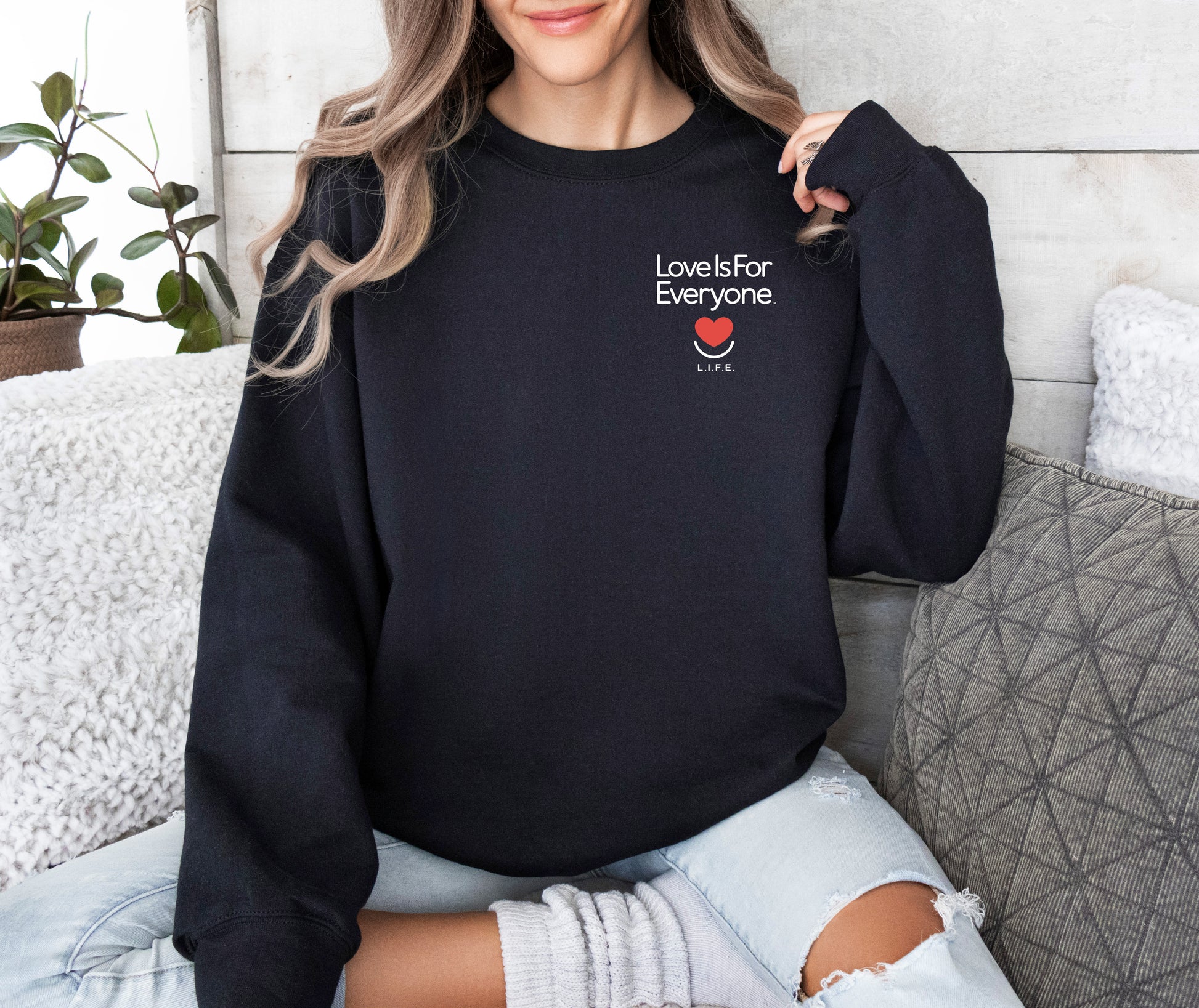 Woman wearing black L.I.F.E. Subtly Stated crewneck with small left-chest heart and "Love is for Everyone" text.