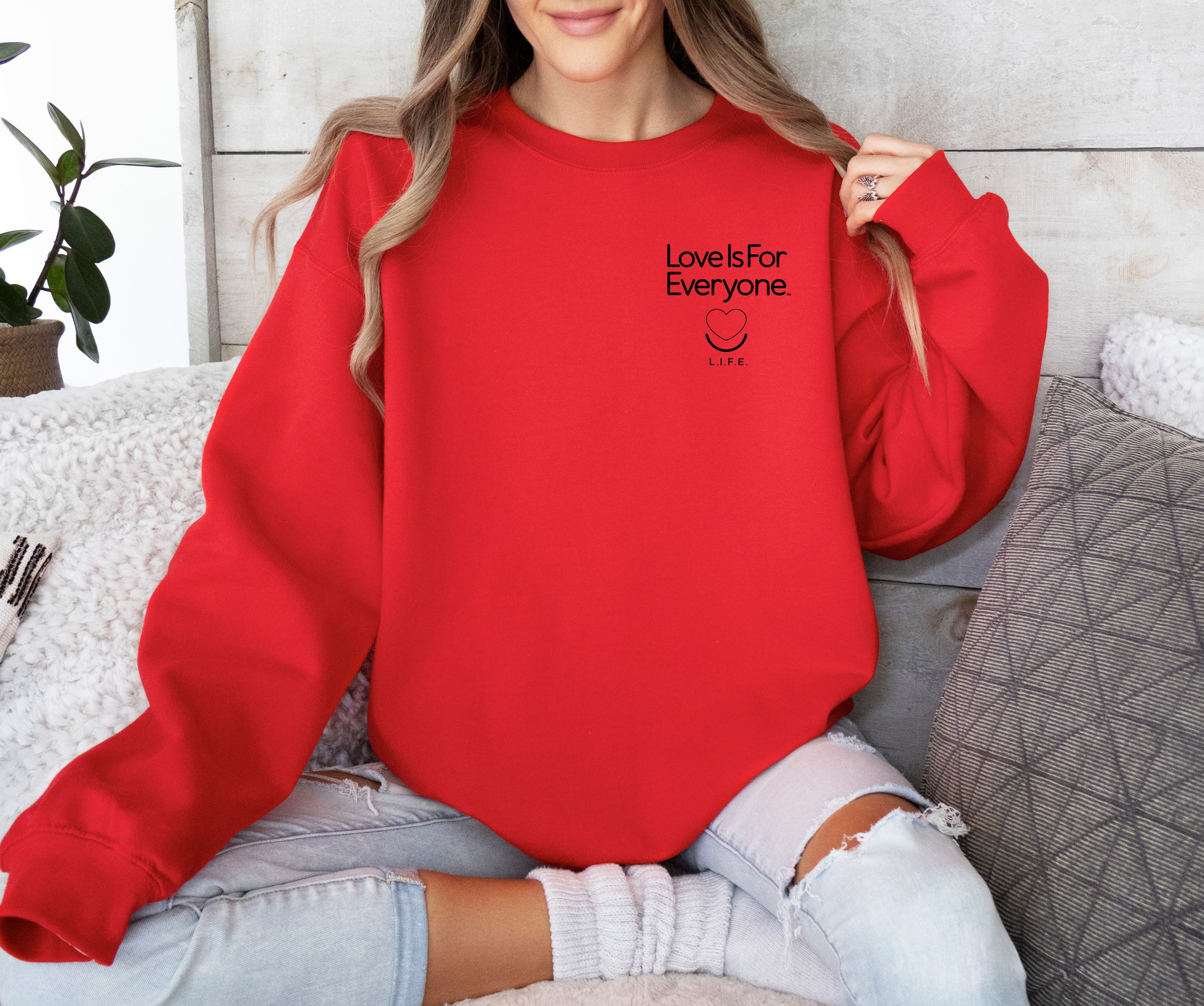Woman wearing red L.I.F.E. Subtly Stated women's/unisex crewneck with left chest logo.